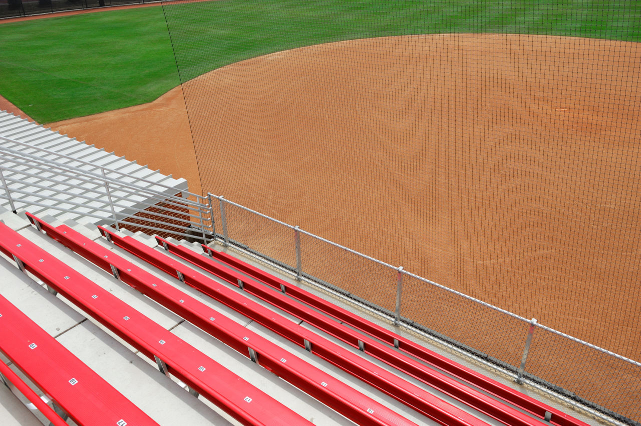 A row of seats are shown behind safety netting at a college baseball stadium.